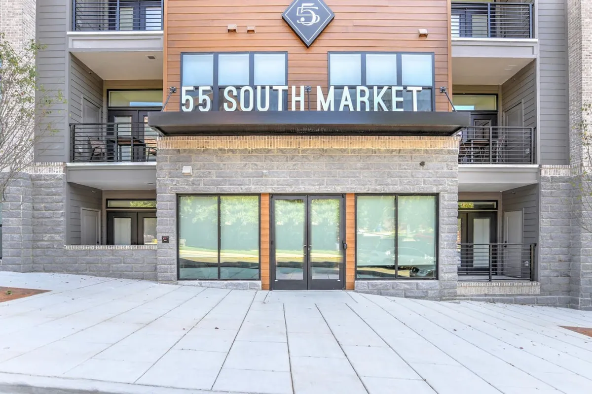 The image presents the building’s modern facade with clear entrance doors and visible signage. The scene is bright and welcoming, showcasing the primary access point for residents. The area around the entrance is clean and well-maintained, providing an immediate urban impression.