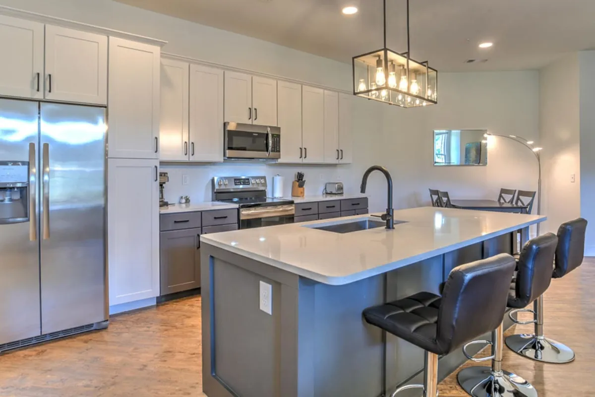 A contemporary kitchen space featuring a large island countertop with bar stools, stainless steel appliances, and elegant pendant lighting. The overall look is clean, modern, and designed for both cooking and casual dining, emphasizing the home's new appliances and updated style.