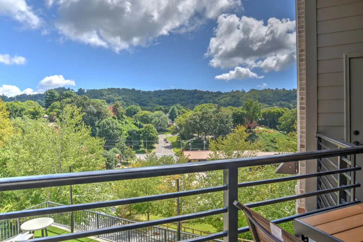 A serene balcony scene overlooking a sweeping mountainous landscape beyond Asheville’s vibrant cityscape. The balcony features a sturdy railing and lush greenery, with soft morning light illuminating the space. A coffee cup rests on a small table, inviting relaxation and quiet contemplation. The atmosphere is tranquil, with hints of daily life such as reading, yoga, or simply enjoying the fresh air.