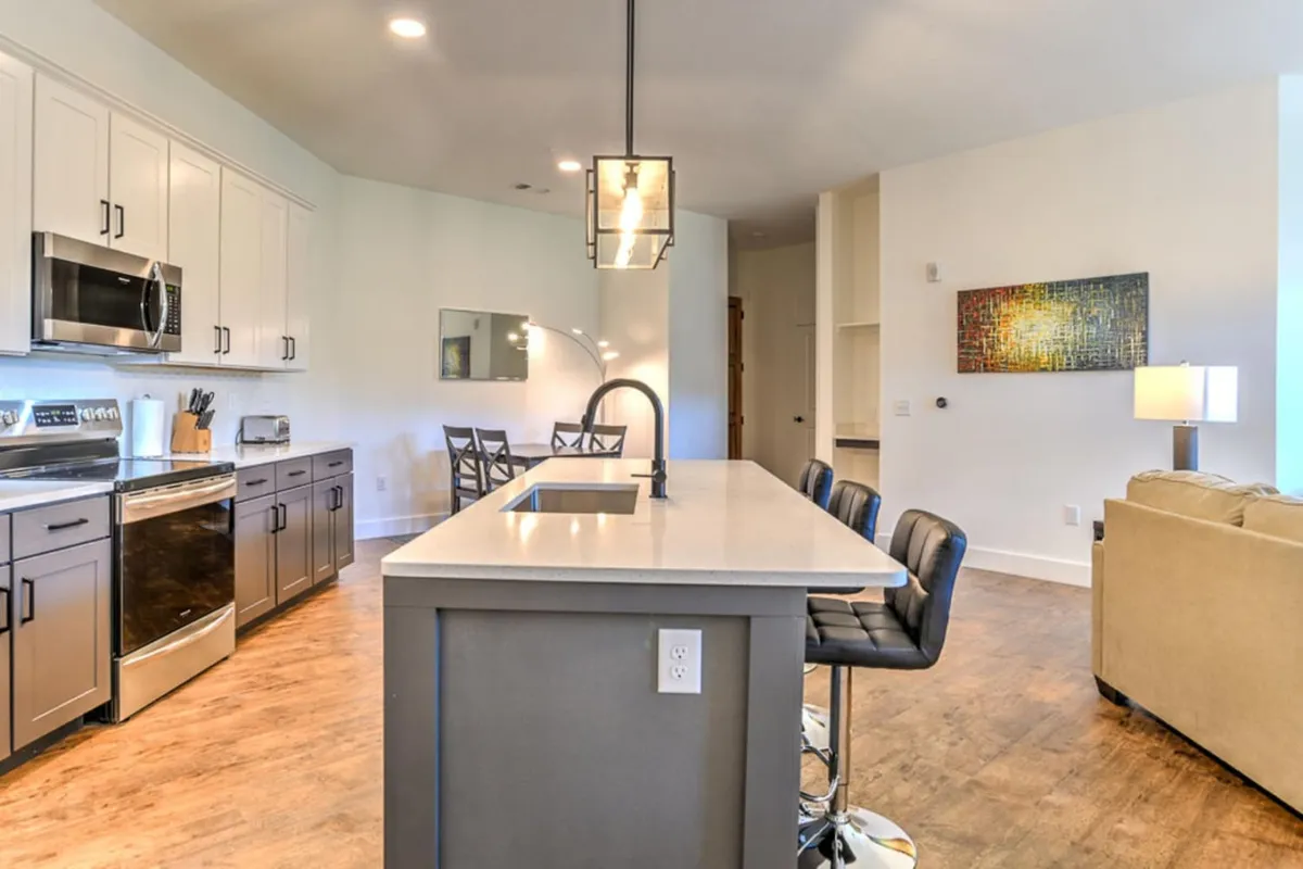 An interior view focusing on the kitchen island, bar stools, sleek stainless steel appliances, and a contemporary art piece. The setting is modern and cozy, evoking a sense of arrival into a private, stylish downtown home.
