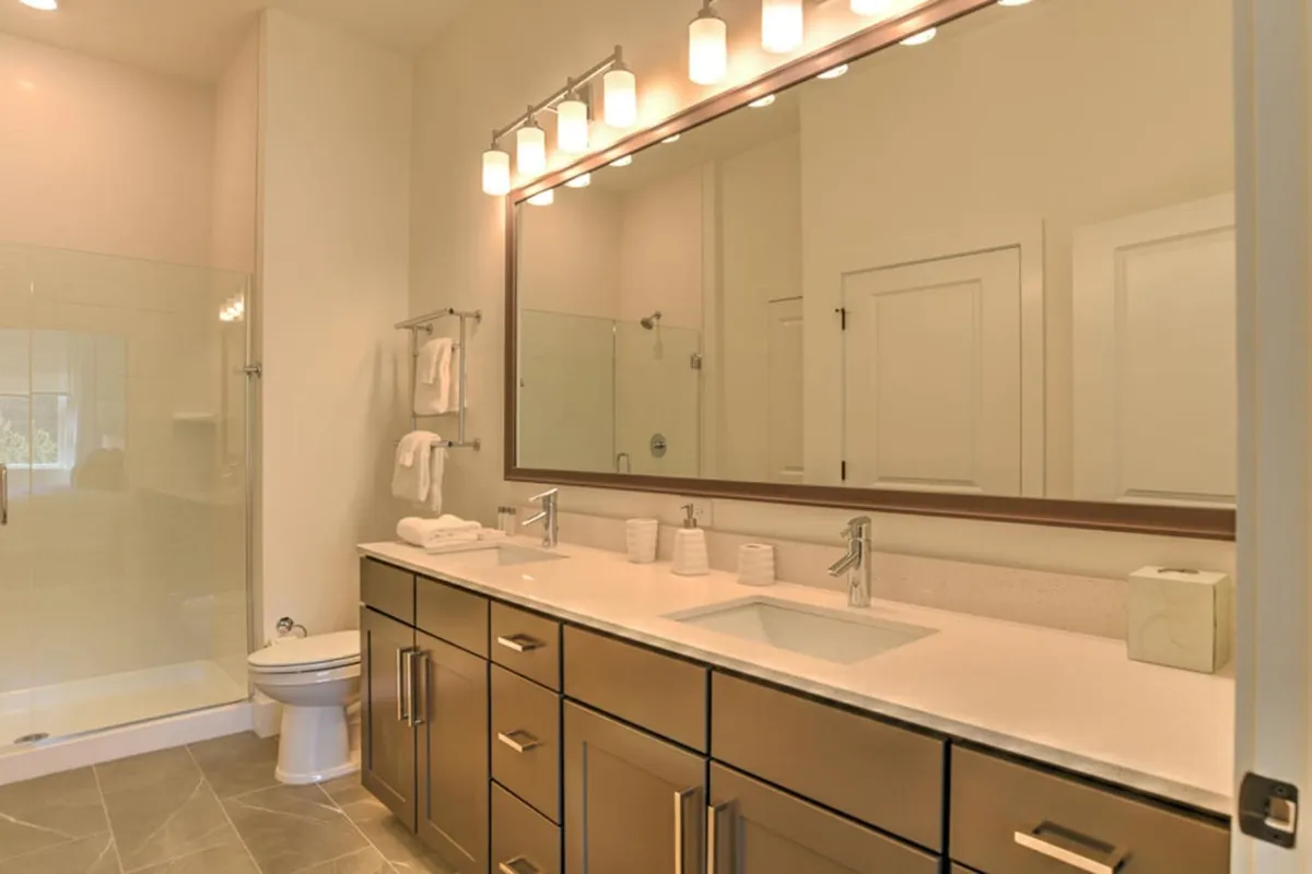 A modern bathroom with a double sink vanity, expansive mirror, and a glass-enclosed shower area. Soft morning light streams in, creating a spa-like, revitalizing setting.
