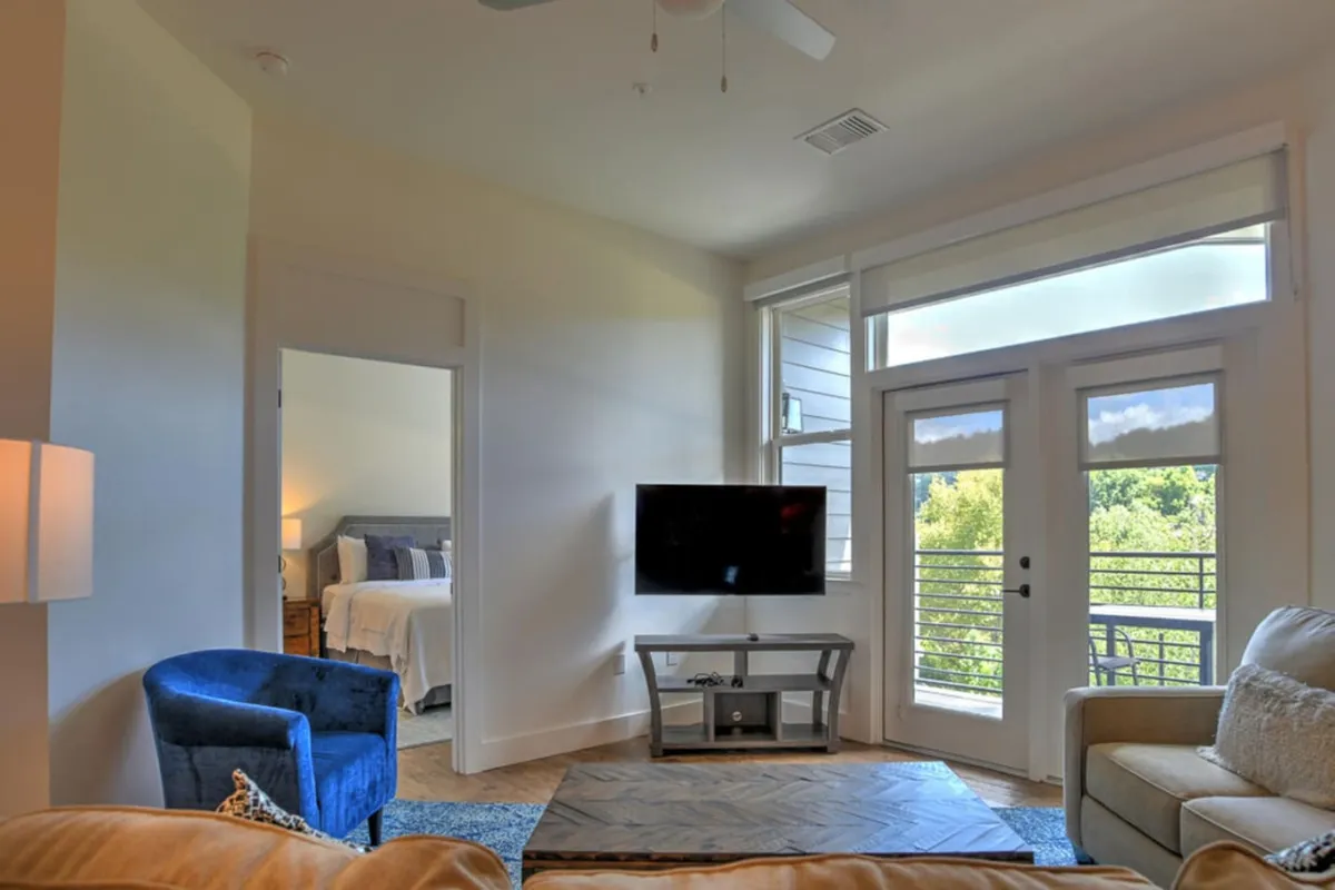 This image showcases a welcoming living area with a sofa, blue chair, and large windows that invite in ample natural light. The windows suggest a connection to the world outside and hint at the vibrant city life and walkability just steps from the condo.