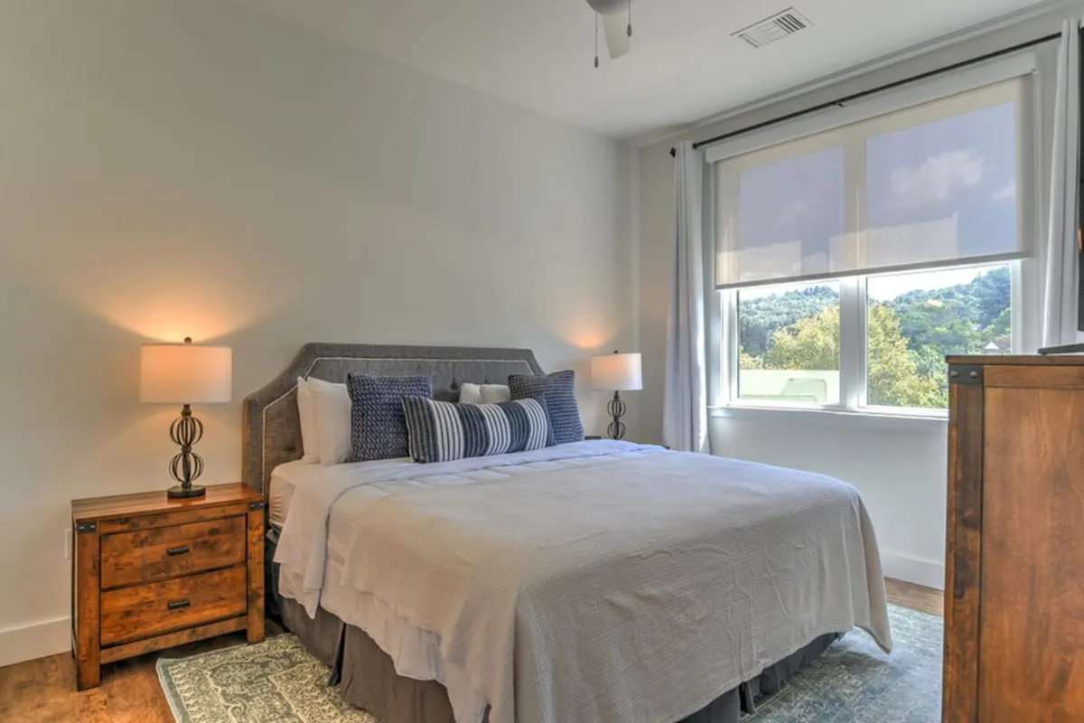 A tranquil bedroom featuring a neatly made bed with soft bedding, stylish nightstands with lamps, and a window that allows natural light to pour in. The scene exudes serenity, inviting relaxation and restful sleep.